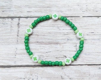 May include: A green beaded bracelet with white clover-shaped beads. The bracelet features a mix of light and dark green beads, creating a festive accessory. The bracelet is designed to be stretchy and comfortable.