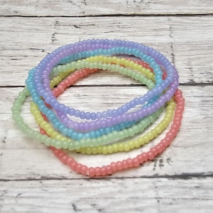 May include: A set of six pastel-colored beaded bracelets. The bracelets are made of small, round beads in shades of pink, yellow, green, and blue.