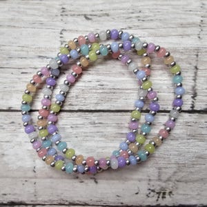 May include: A set of three pastel-colored beaded bracelets with silver beads. The bracelets are layered on top of each other and are made with small, round beads.