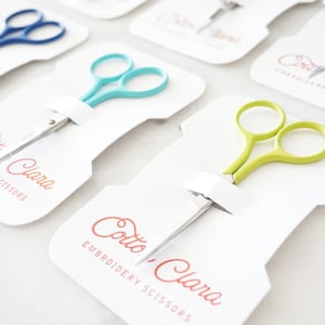 May include: Three different pairs of embroidery scissors in individual packaging. The scissors are turquoise, green, and blue. The packaging is white with the text "Cotto Clara Embroidery Scissors" printed in red.