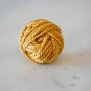 May include: A ball of yellow yarn, tightly wound and ready for knitting or crocheting.