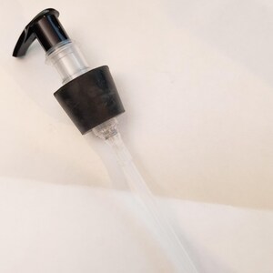 May include: A clear plastic pump dispenser with a black top and a long clear tube.