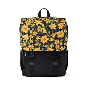 May include: Black backpack with a flap featuring a yellow lily floral pattern on a dark background. The backpack has a top handle, adjustable straps, and two front buckles. A small metal emblem is centered on the front.