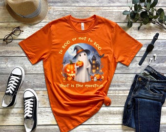 May include: Orange Halloween-themed t-shirt with a graphic of a ghost holding a pumpkin, a haunted house, and the text "To boo, or not to boo... That is the question." Black and white sneakers and blue jeans are also in the image.