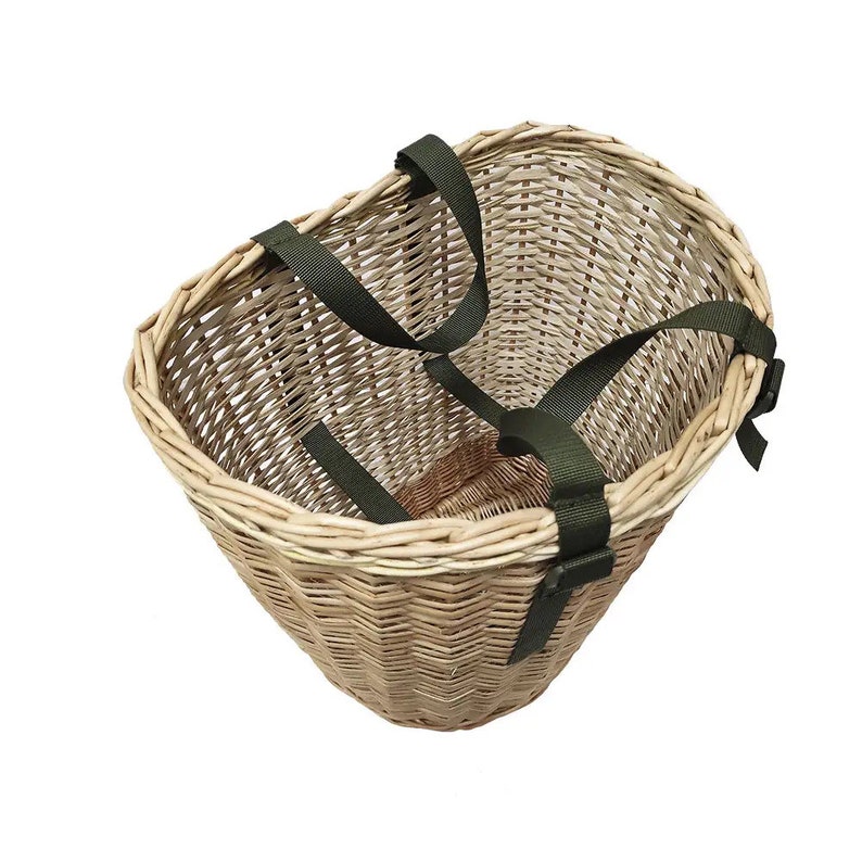 May include: A wicker basket with green straps. The basket is oval shaped and has a woven pattern. The straps are adjustable and have buckles.