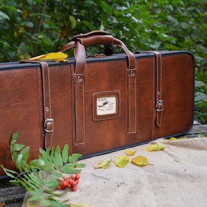 May include: A brown leather gun case with a carrying handle and two buckles. The case has a label with the text "Borealis Hunting Outfitters" on it.