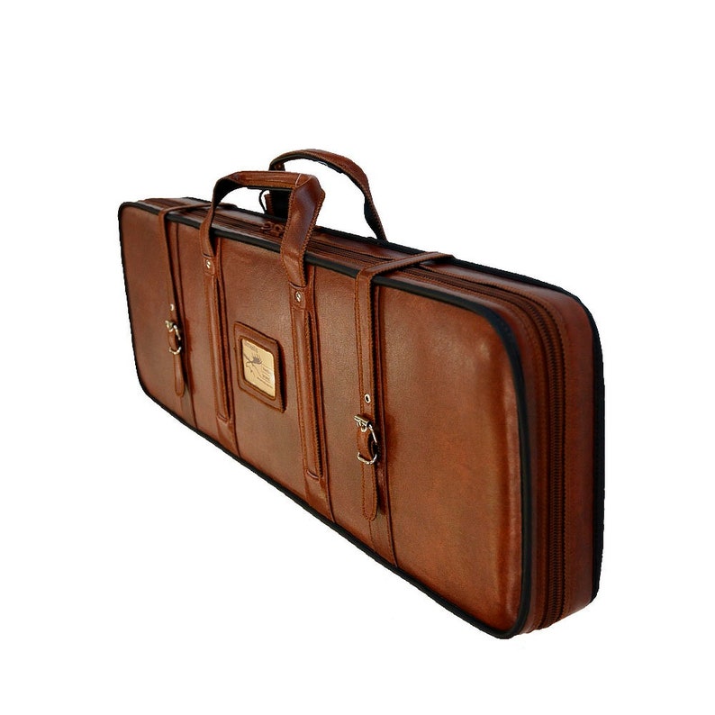 May include: A brown leather case with a zipper closure and a handle. The case has a metal buckle and a nameplate.