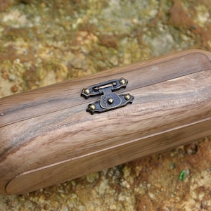 May include: A wooden box with a brass latch and decorative accents. The box is closed and has a natural wood grain.