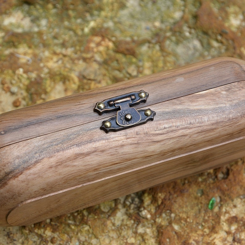 May include: A wooden box with a brass latch and decorative accents. The box is closed and has a natural wood grain.