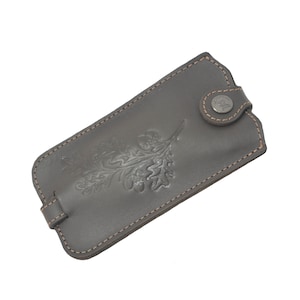 May include: A brown leather key chain with a stitched edge and a metal button. The key chain has an embossed design of an oak leaf.