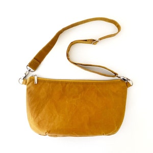 May include: A mustard yellow crossbody bag with a long adjustable strap and a zipper closure.