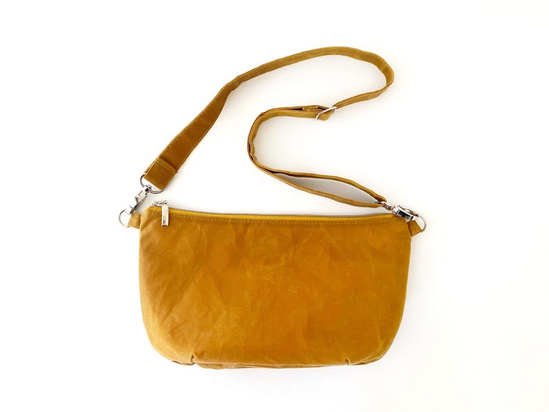 May include: A mustard yellow crossbody bag with a long adjustable strap and a zipper closure.