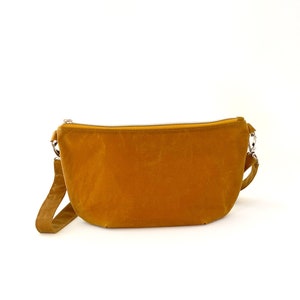 May include: A mustard yellow crossbody bag with a zipper closure and a long strap.