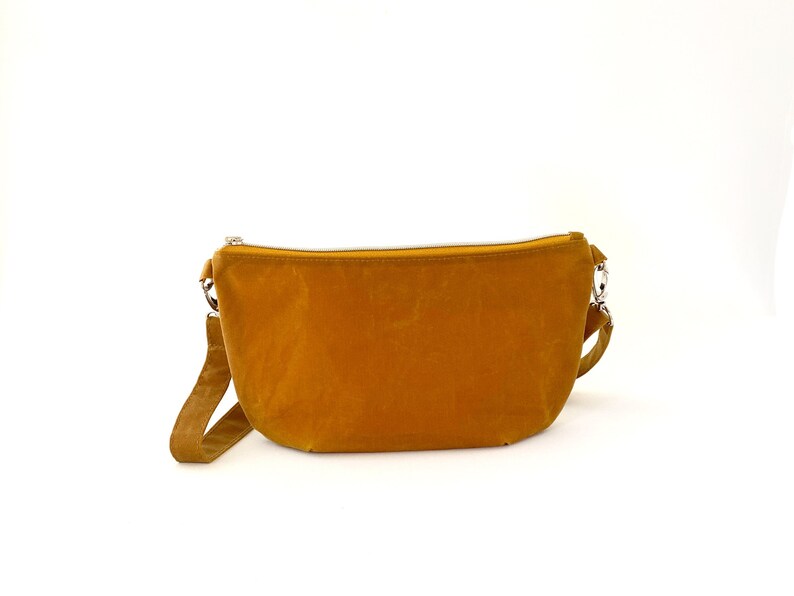 May include: A mustard yellow crossbody bag with a zipper closure and a long strap.