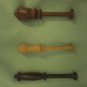 May include: Three wooden knitting needles with different coloured wood finishes. The needles are approximately 15 cm long.