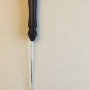 May include: A black plastic handle with a metal hook attached to the end. The hook is bent into a small loop.