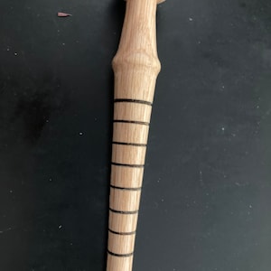 May include: A wooden bottle stopper with a rounded top and a long, tapered body. The body features several black bands. The stopper is made of light-colored wood and is designed to fit into a bottle.