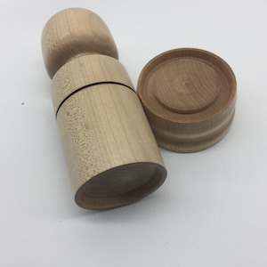 May include: A set of two wooden containers, one tall and cylindrical with a rounded top, and the other a shorter, round lid. Both are made of light-coloured wood with a natural grain.