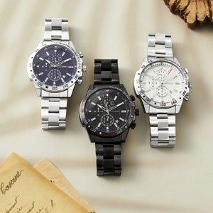May include: Three wristwatches with chronograph features. The watches have silver, black, and white faces with black, silver, and black bands respectively. Each watch has a tachymeter scale around the outer edge of the face.