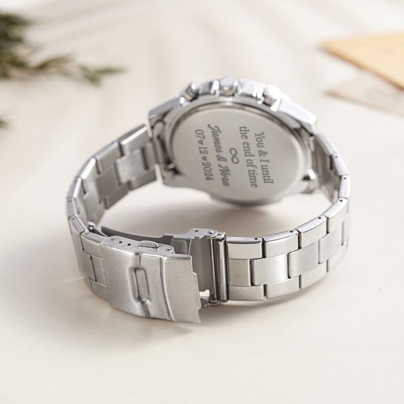 May include: Silver wristwatch with a stainless steel strap. The back of the watch has an inscription that reads "You & I until the end of time &infin; James & Nova 07/12/2024".