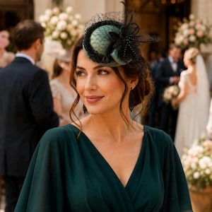Könnte beinhalten: Ein dunkelgrüner Fascinator mit abgerundeter Krone, schwarzem Netz und dekorativen schwarzen Federn. Das Kopfstück wird mit einem dunkelgrünen Kleid mit V-Ausschnitt und flatternden Ärmeln kombiniert, ergänzt durch lange schwarze Ohrhänger.
