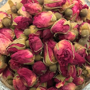 May include: A glass bowl filled with dried rose buds, with additional rose buds scattered on a wooden surface.
