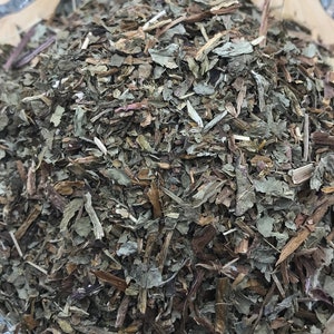 May include: A glass bowl filled with dried green and brown herbs. The herbs are a mix of leaves and stems.