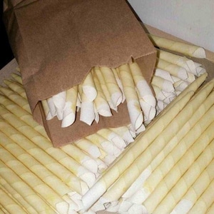May include: A brown paper bag filled with a large quantity of beige ear candles. The candles are made of a natural material and are designed to be used for earwax removal.