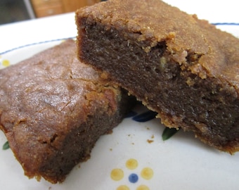 May include: Two square-cut brownies with a rich, dark brown interior and a lighter, golden-brown crust. The brownies are on a decorative plate with a blue and yellow floral pattern. The texture appears moist and dense.