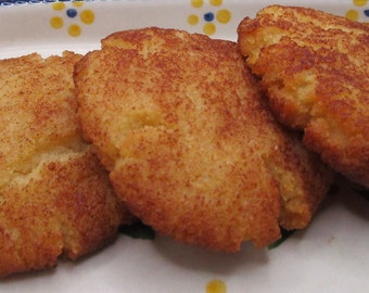 Puede incluir: Tres galletas redondas horneadas de color marrón dorado con una superficie texturizada y ligeramente agrietada espolvoreada con una especia de color marrón rojizo, dispuestas en fila sobre una bandeja ovalada de cerámica blanca con flores.