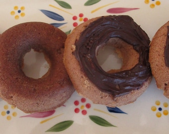 May include: Four chocolate frosted donuts on a decorative oval plate. The donuts are light brown with a dark chocolate frosting. The plate has a white background with a floral pattern in yellow, blue, and red.