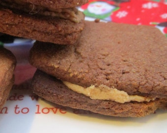 May include: Close-up of stacked, square-shaped cookies with a light-colored filling. The cookies are a rich brown color, and the filling appears to be a creamy tan. The cookies are stacked on a white plate with red text that says "made with love".