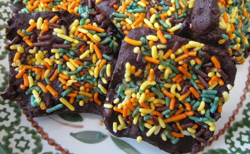 Puede incluir: Primer plano de trozos de corteza de chocolate cubiertos de chispas de colores. La corteza es de color marr&oacute;n oscuro y las chispas son amarillas, naranjas, verdes y marrones. Las piezas est&aacute;n dispuestas sobre un plato decorativo.