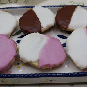 May include: Six black and white cookies on a decorative oval plate. Three cookies have a white and chocolate frosting, and three have white and pink frosting. The plate has a blue and white floral design.