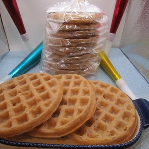 May include: Four golden brown waffles in a blue and white ceramic dish. The waffles are stacked on top of each other. There are also several packages of cookies in the background.