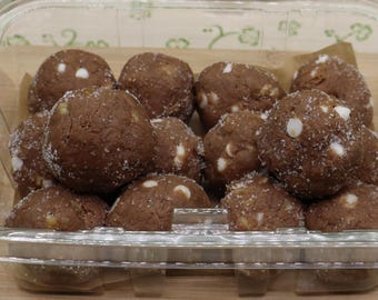 May include: A clear plastic container filled with twelve round, brown chocolate cookie dough balls. Each dough ball is speckled with small white chocolate chips and a light dusting of granulated sugar, arranged in a grid pattern inside the box.