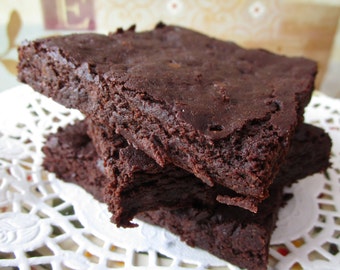 Peut inclure: Gros plan sur trois brownies au chocolat noir empilés sur une nappe blanche et dentelle. Les brownies ont une surface riche et texturée et semblent fraîchement cuits. L'image met en évidence l'aspect moelleux et fondant des friandises.
