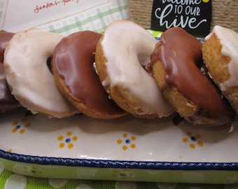 May include: A rectangular ceramic serving dish with a blue rim and yellow and blue floral accents holds six ring-shaped donuts. Three donuts are coated in smooth chocolate icing, and three are covered in a translucent white sugar glaze.