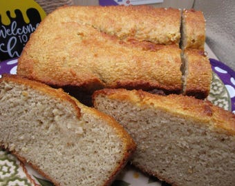 May include: A loaf of golden-brown baked bread with a textured, crusty top, sliced into several pieces. The interior of the bread is light beige with a dense, porous crumb structure. The bread is displayed on a patterned plate with a floral design.