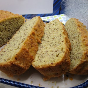 May include: Sliced loaf of bread with a golden-brown crust and a light-colored interior speckled with seeds. The bread is presented on a decorative, rectangular plate with a blue and white floral pattern.
