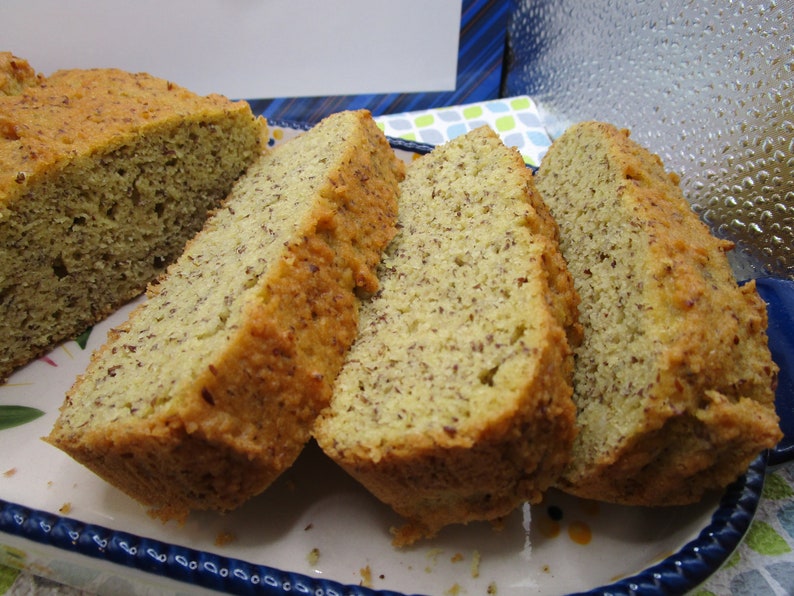 May include: Sliced loaf of bread with a golden-brown crust and a light-colored interior speckled with seeds. The bread is presented on a decorative, rectangular plate with a blue and white floral pattern.
