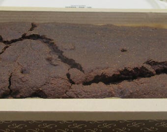 May include: A dark brown loaf of bread in a cardboard box with a green and brown patterned design.