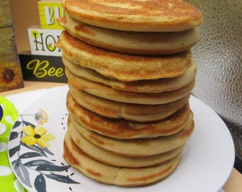Peut inclure: Une haute pile de neuf crêpes rondes dorées servies sur une assiette blanche décorée d'un motif de fleur jaune et de feuilles gris foncé. Les crêpes présentent une surface lisse et cuite avec des bords légèrement plus foncés.