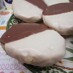 May include: Close-up of several black and white cookies on a decorative plate. Each cookie is round and covered with a white icing on one half and a dark chocolate icing on the other half. The cookies are a classic bakery treat.