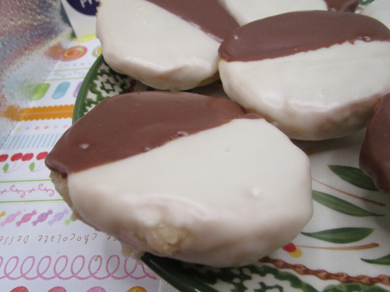 May include: Close-up of several black and white cookies on a decorative plate. Each cookie is round and covered with a white icing on one half and a dark chocolate icing on the other half. The cookies are a classic bakery treat.
