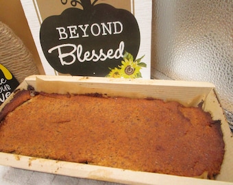 May include: A loaf of freshly baked bread in a wooden loaf pan. The bread is golden brown and has a slightly rough texture. The pan is made of light wood and has a simple design.