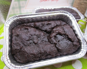 May include: Close-up of several dark brown baked goods in rectangular foil containers. The baked goods have a textured surface and appear to be freshly baked. The containers are arranged on a green and white surface.