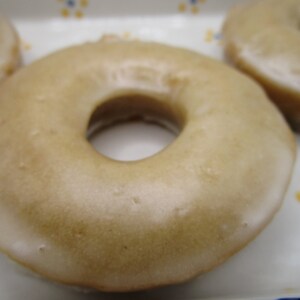 May include: Close-up of glazed donuts. The donuts have a light brown glaze and a hole in the center. The donuts are on a white plate with a blue and yellow floral design.