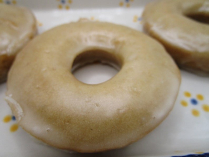 May include: Close-up of glazed donuts. The donuts have a light brown glaze and a hole in the center. The donuts are on a white plate with a blue and yellow floral design.