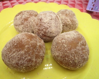 May include: Five powdered sugar-covered donut holes on a bright yellow plate. The donuts are golden brown with a light dusting of white powder. The plate has a scalloped edge, and the background includes a red and white checkered tablecloth.